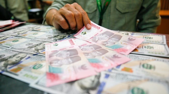 Petugas salah satu tempat penukaran mata uang asing menunjukkan uang rupiah dan dollar AS di Jakarta, Selasa (19/5/2026). [Suara.com/Alfian Winanto]